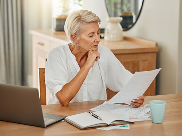 woman sitting at table looking through documents with laptop and mug nearby